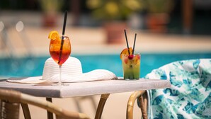 Two cocktails on a table by a poolside with a wicker chair and a white hat. - Hotel Califfo (Quartu Sant'Elena)
