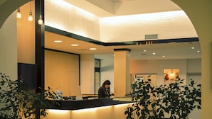A reception area with a counter, potted plants, and a person behind the counter. - Hotel Califfo (Quartu Sant'Elena)