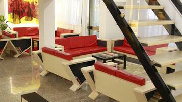 A modern lobby with red and white furniture, a staircase, and a large window with curtains.