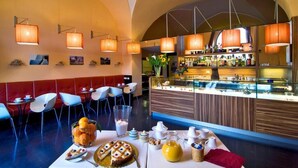 Un restaurant moderne doté d’un bar, avec un îlot central sur lequel est disposée une vitrine réfrigérée, des tables et des chaises, et un éclairage suspendu.