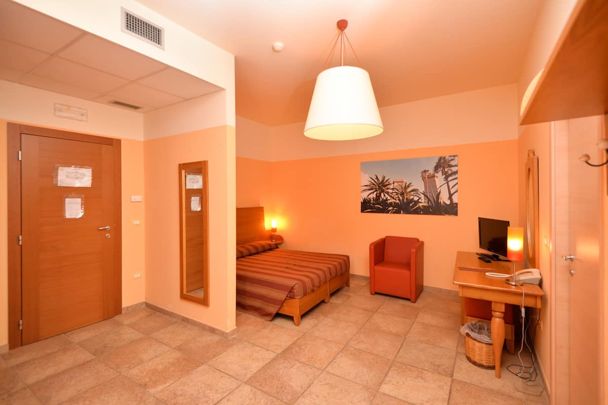 Une chambre d’hôtel avec un lit, un bureau avec un ordinateur, une chaise, une lampe et un tableau au mur.