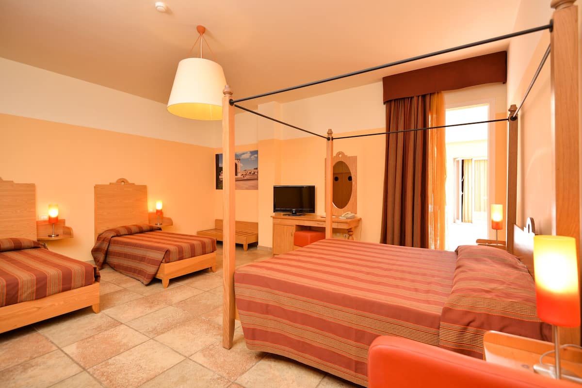Une chambre d’hôtel avec un grand lit, deux petits lits, un bureau avec une télévision, un miroir et une fenêtre avec des rideaux.