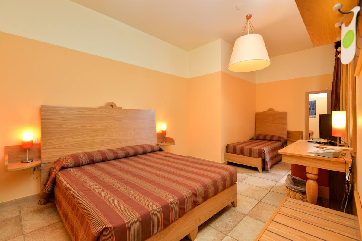 Une chambre avec deux lits, une tête de lit en bois, des lampes de chevet, un bureau avec une chaise et un luminaire suspendu.