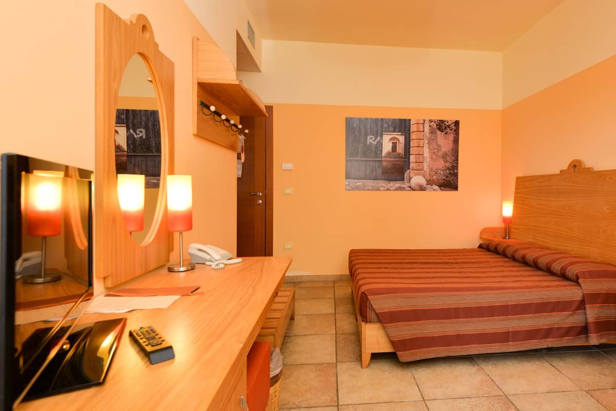 Une chambre d’hôtel avec un bureau en bois, un lit avec une literie à rayures, un grand miroir et un tableau accroché au mur.