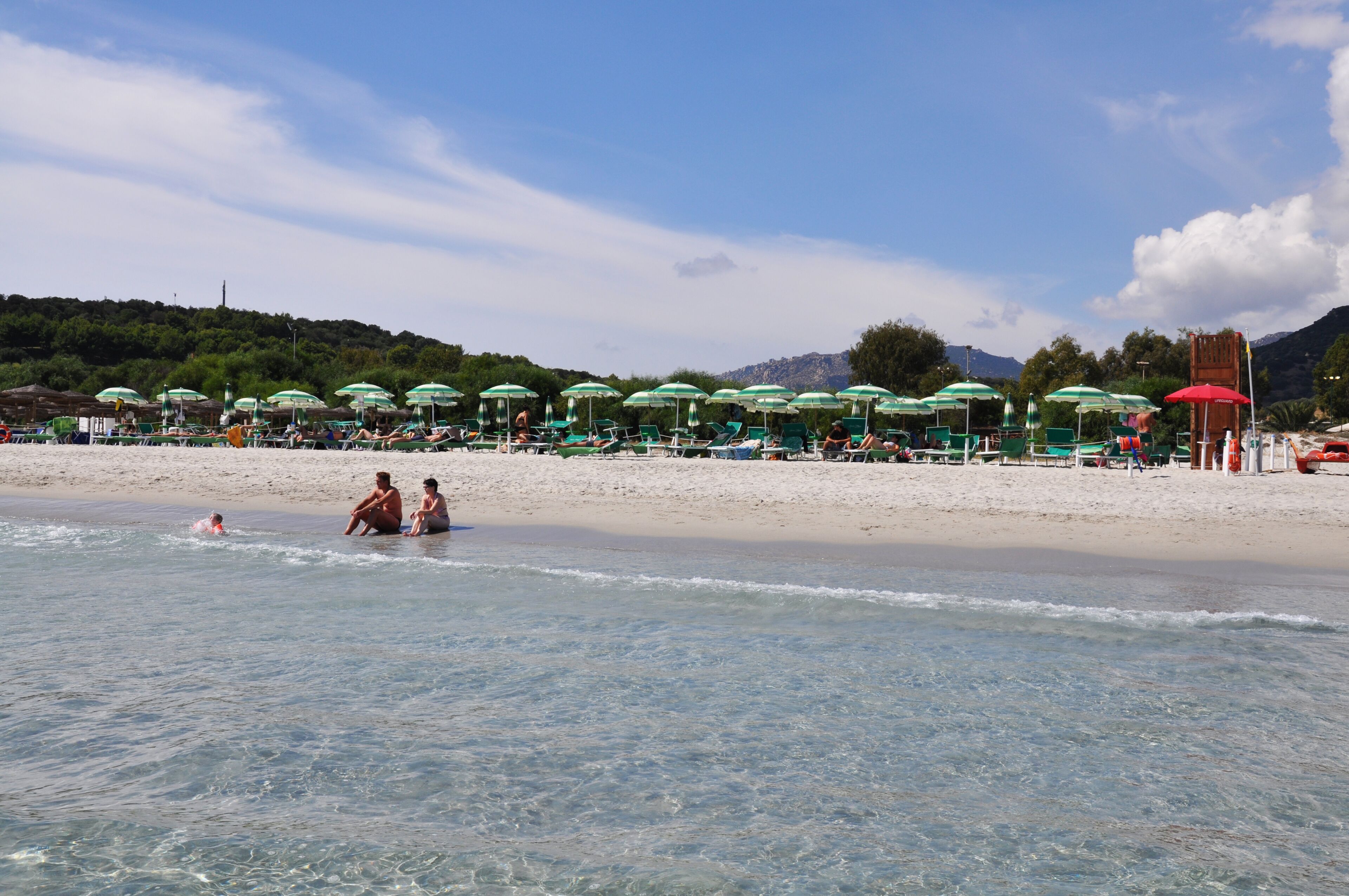Una playa con agua cristalina, sombrillas y gente.