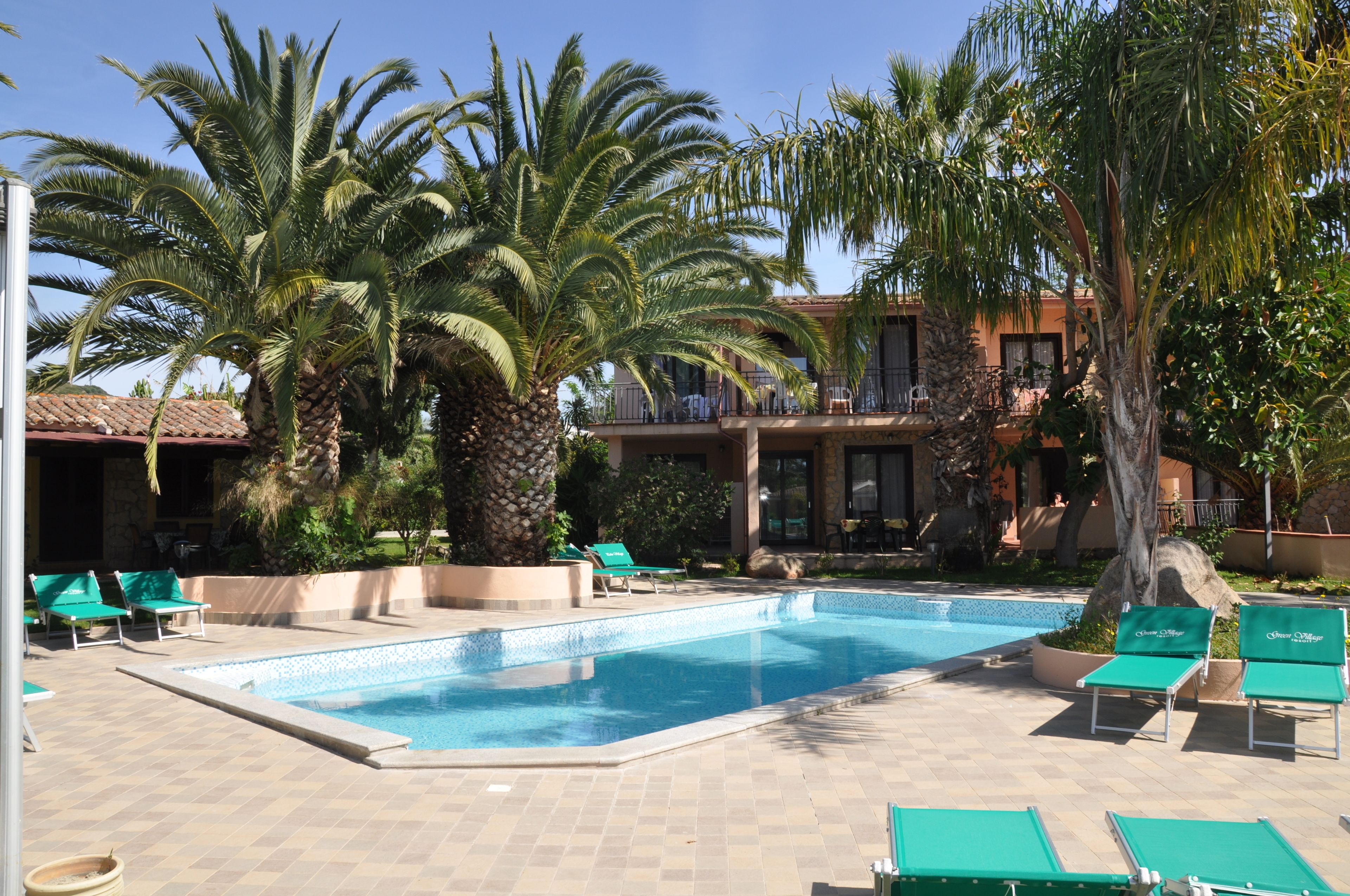 A swimming pool with lounge chairs, palm trees, and a building with balconies.