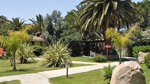 A garden pathway leading to a building with a yellow facade, surrounded by various plants and a large rock. - Green Village Resort (Villasimius)