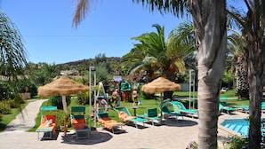 A poolside area with lounge chairs, a thatched umbrella, and a pool. - Green Village Resort (Villasimius)