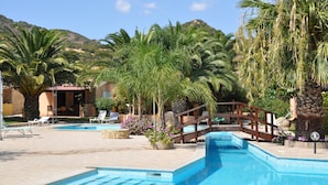 A pool area with multiple swimming pools, lounge chairs, and palm trees. - Green Village Resort (Villasimius)