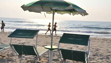 Sillas de playa y una sombrilla en una arena arenosa con el océano al fondo.