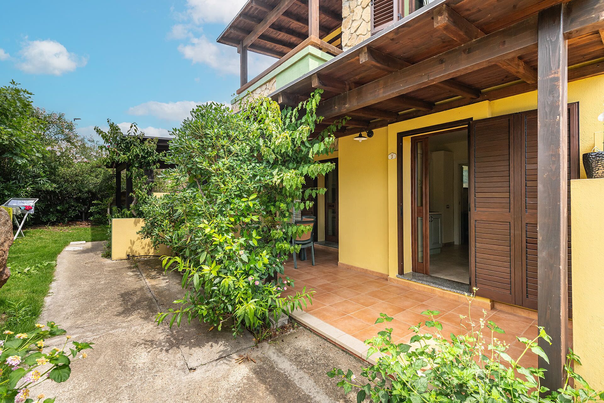 A two-story house with a yellow exterior, a wooden porch, and a green garden.