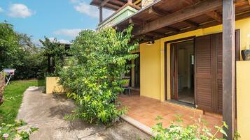 Une maison à deux étages, avec une façade jaune, une véranda en bois et un jardin verdoyant.