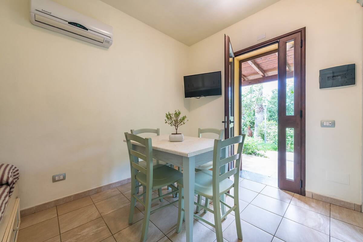 A dining area with a table and chairs, an air conditioning unit, a TV, and a door leading outside.