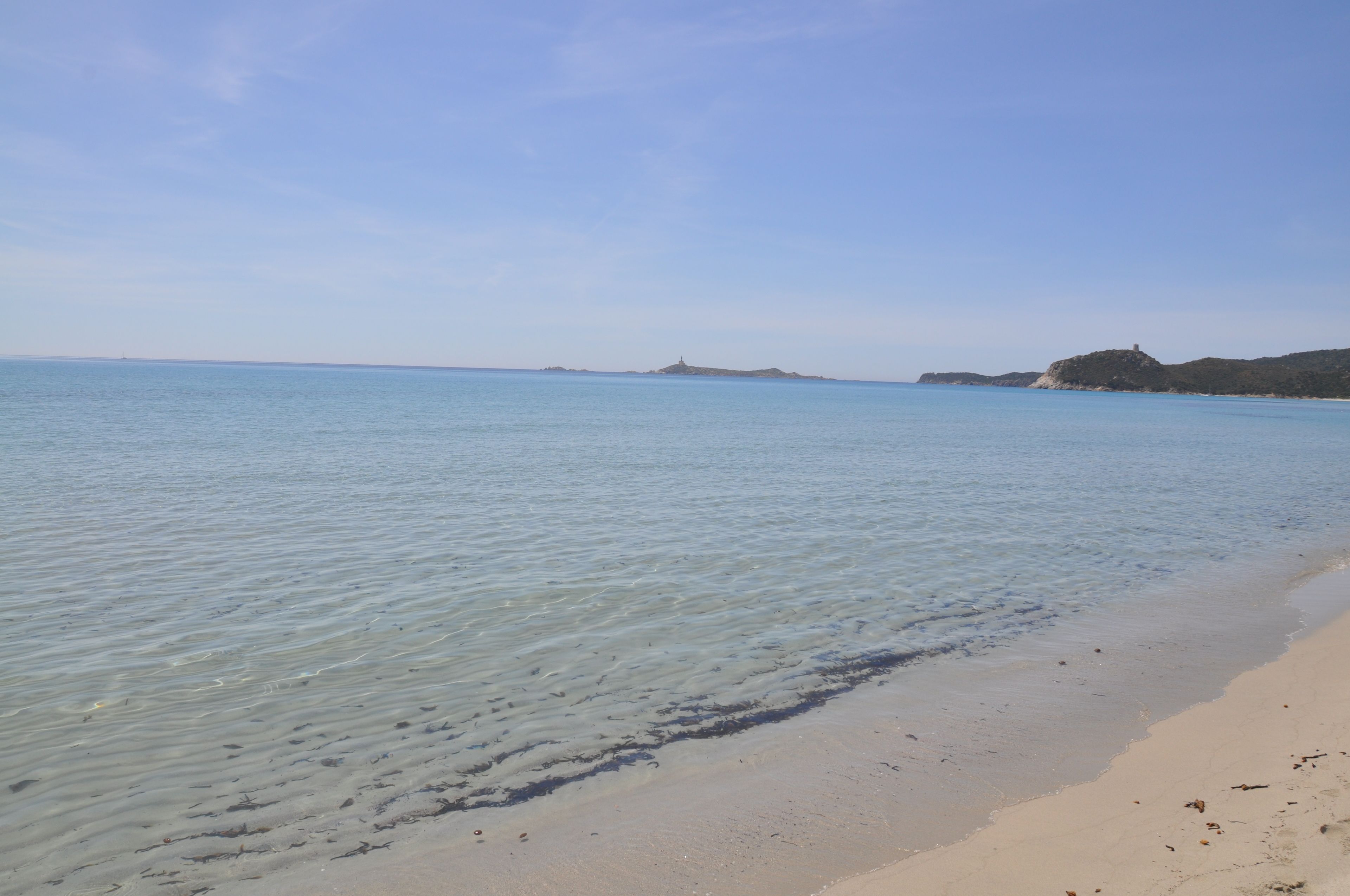 Une plage à l’eau claire, avec un rivage sablonneux et des collines qui se dessinent à l’horizon.
