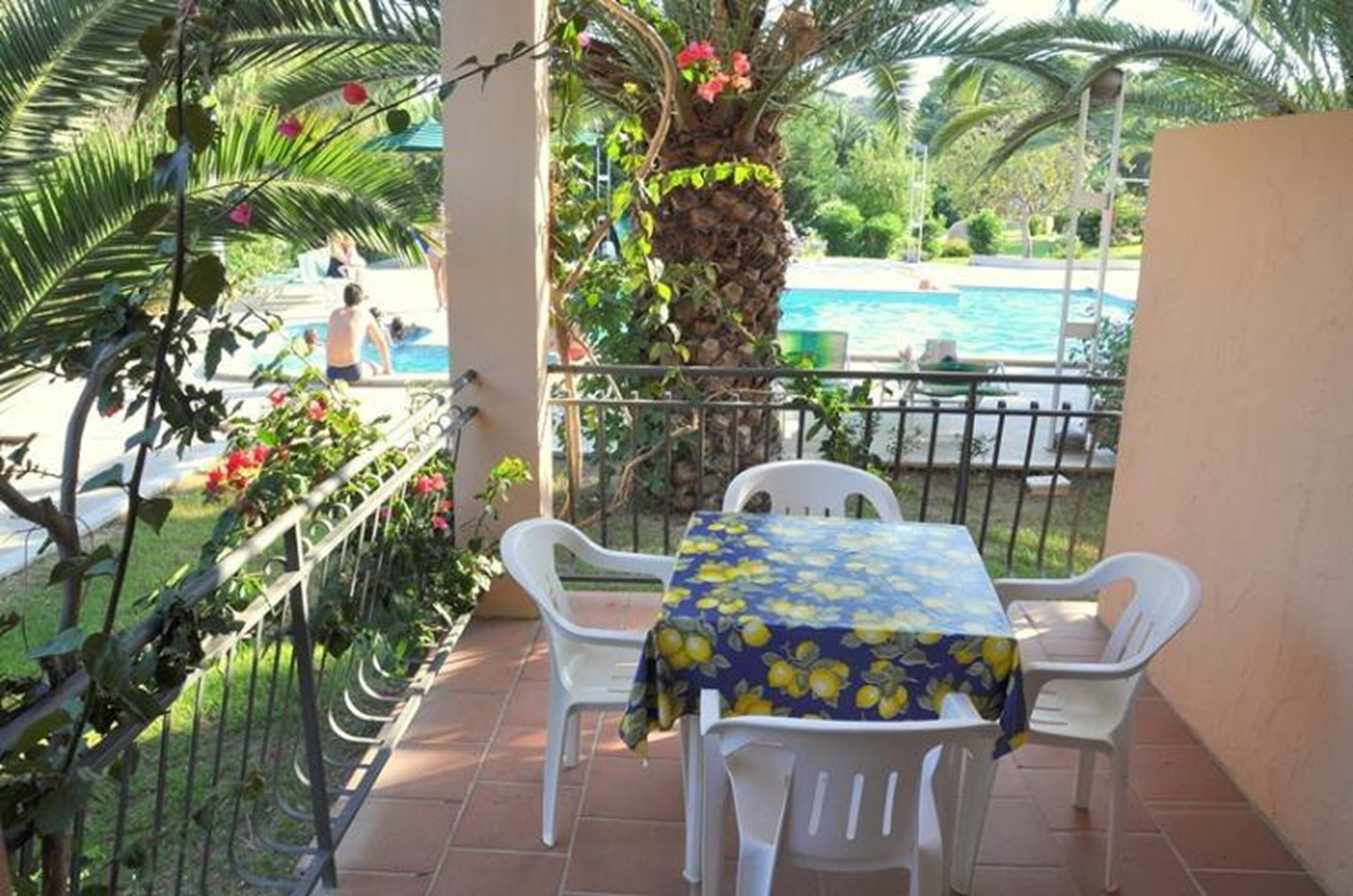 A balcony with a table and chairs, overlooking a swimming pool and lush greenery.