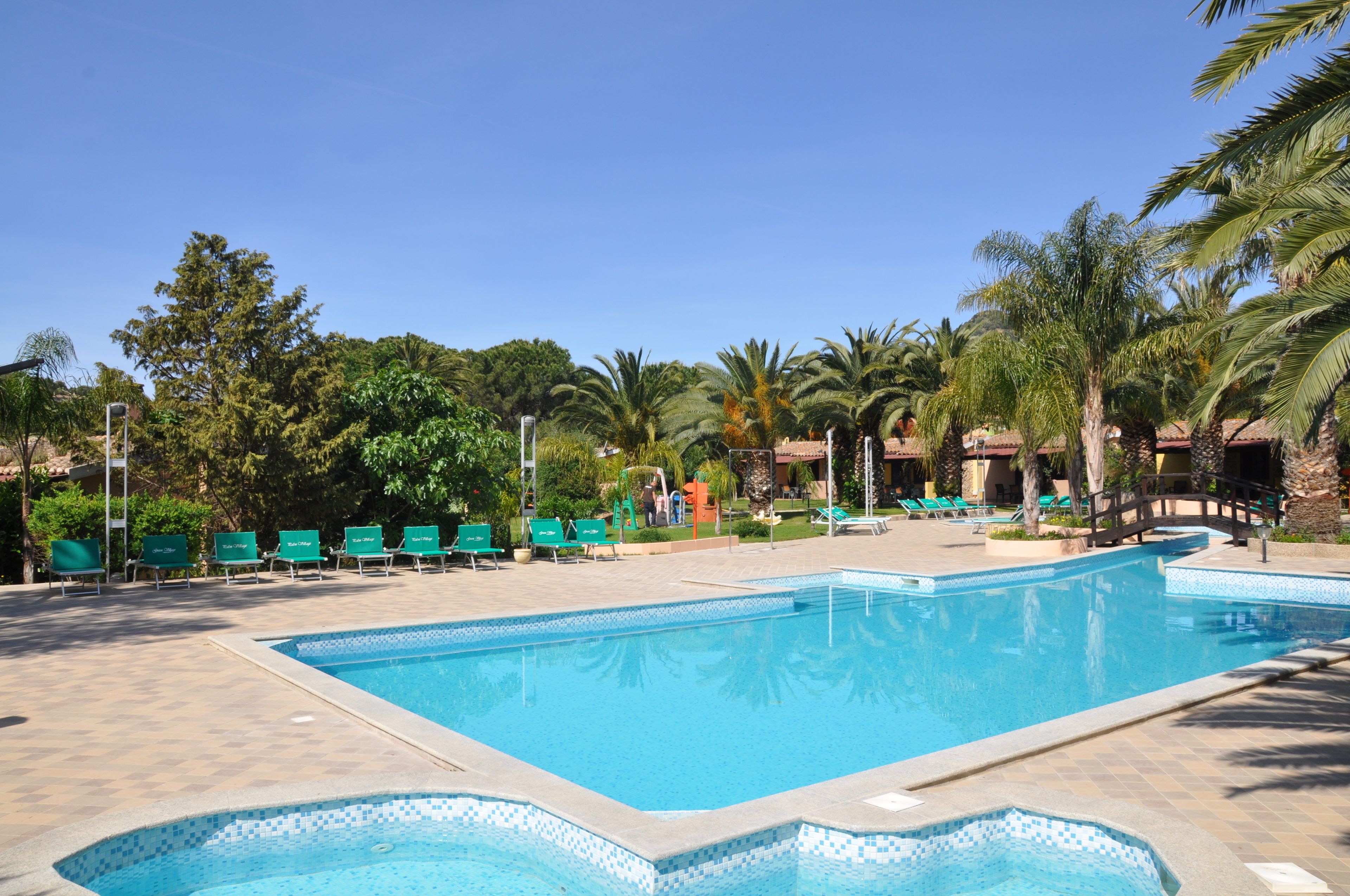 Une piscine dont le bord est revêtu de carrelage, entourée de chaises longues et de palmiers.