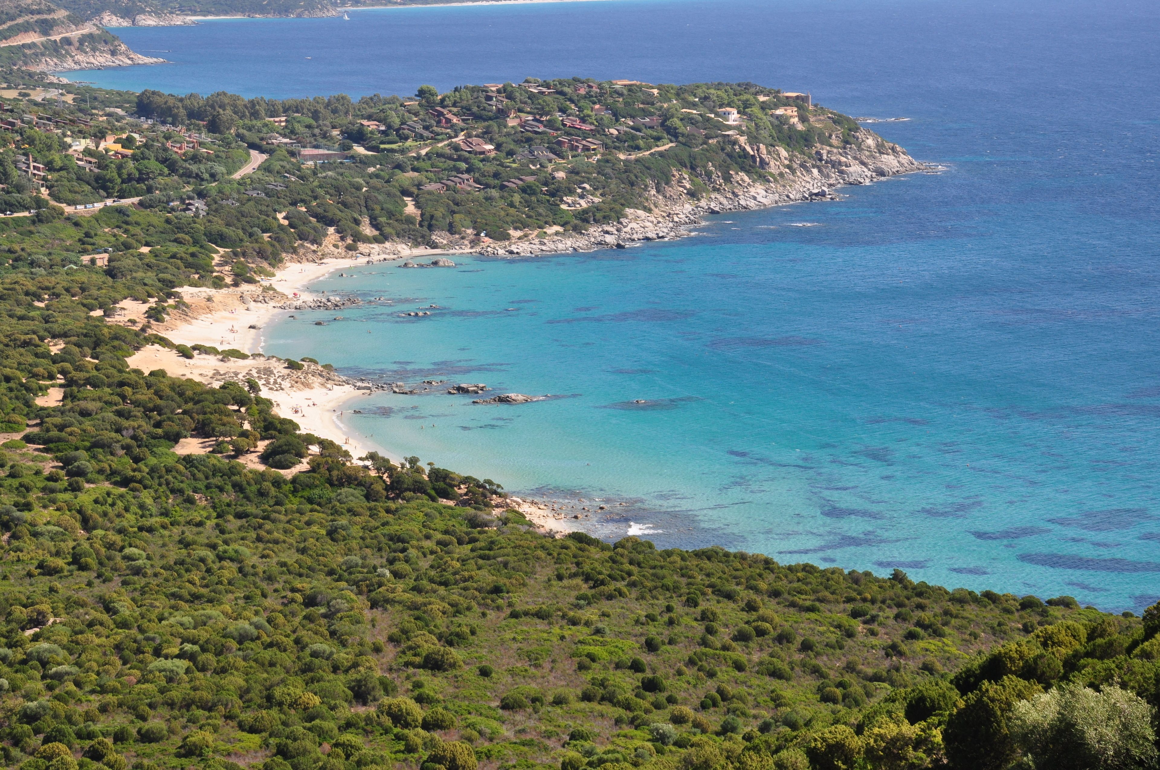Eine Küstenlandschaft mit Strand, üppiger Vegetation und einem kleinen Gebäude auf einem Hügel.