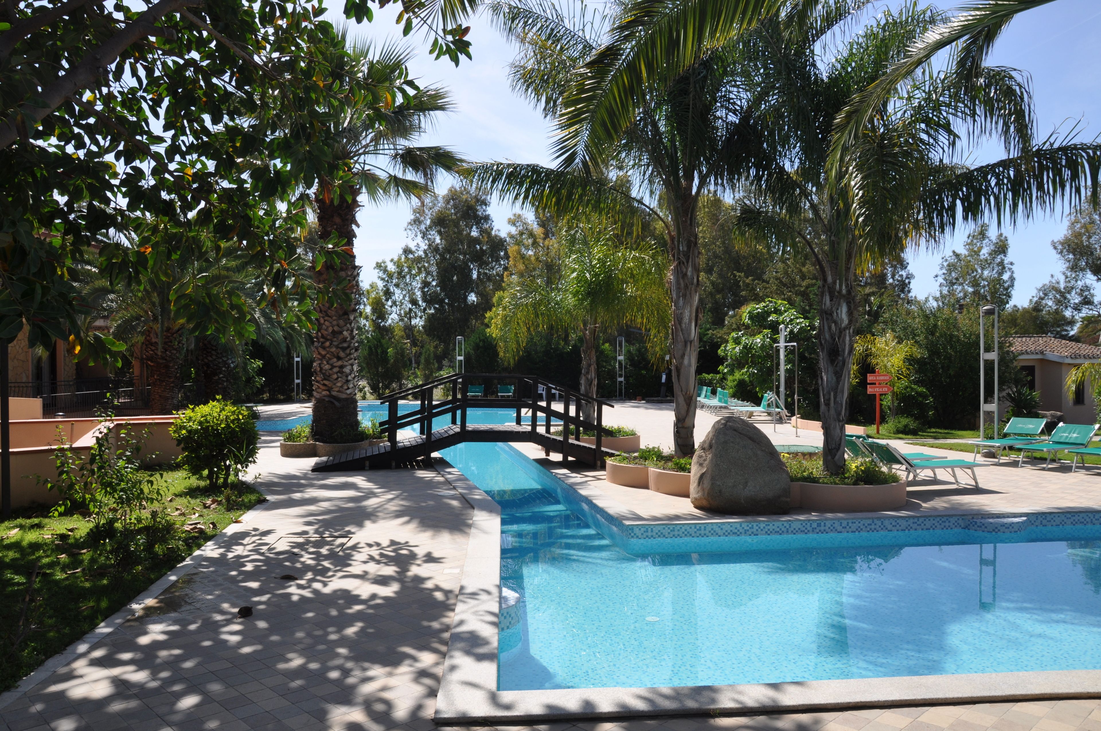 A pool area with a bridge, palm trees, and lounge chairs.