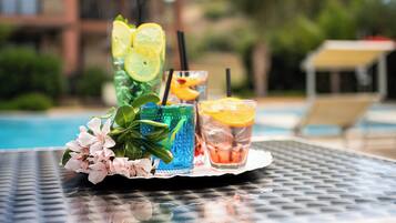Une table avec trois boissons, chacune d’une couleur et d’une garniture différentes, près d’une piscine.