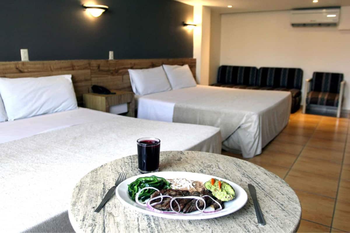 A hotel room with two beds, a dining table with a plate of food and a glass of red wine, and a seating area with chairs.