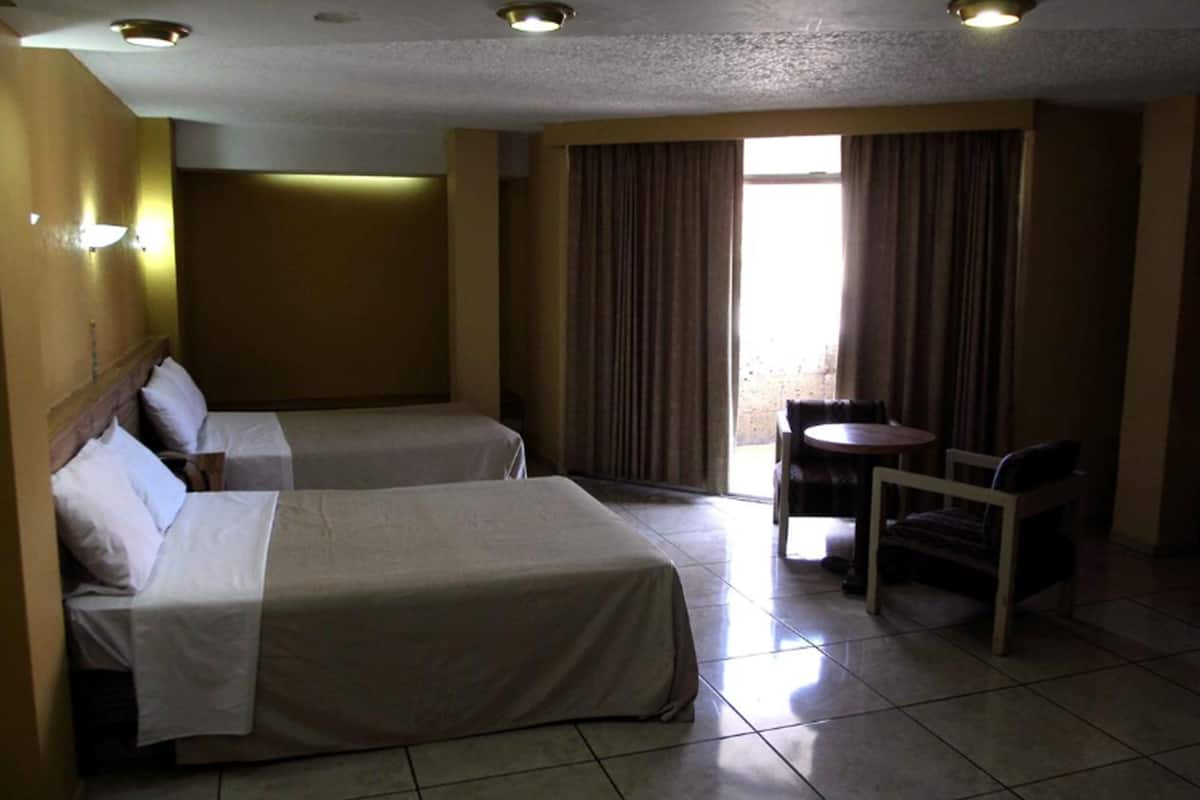A hotel room with two beds, a small table, and a chair.