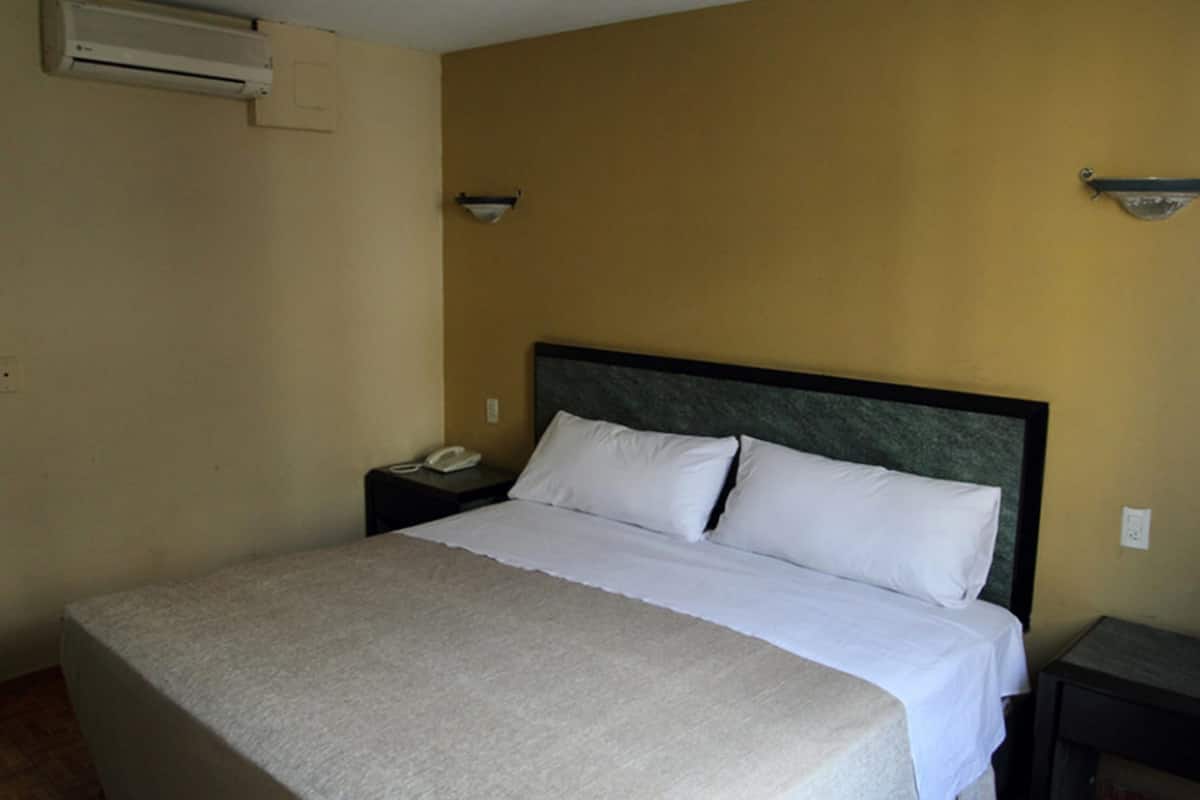 A hotel room with a large bed, a bedside table with a phone, and an air conditioning unit on the wall.