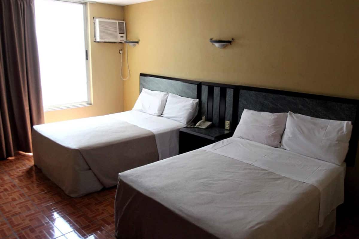 Two single beds with white linens, a bedside telephone, and an air conditioning unit on the wall.