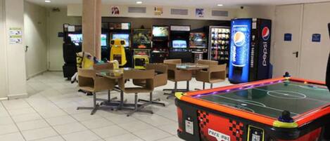 Una habitación con mesa de billar, juegos de arcade y un refrigerador de Pepsi.