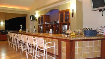 Una zona de bar con una barra larga, varios taburetes altos y un televisor montado en la pared.