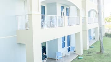 Um hotel com estrutura em dois andares, varandas com grades brancas e uma pequena área externa com cadeiras e uma mesa.