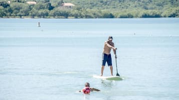 Un hombre y una mujer en una tabla de remo en aguas tranquilas, con una colina boscosa al fondo.
