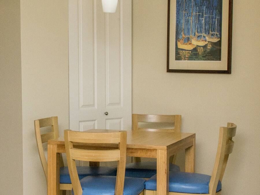 A dining area with a wooden table and chairs, a white door, and a framed painting on the wall.