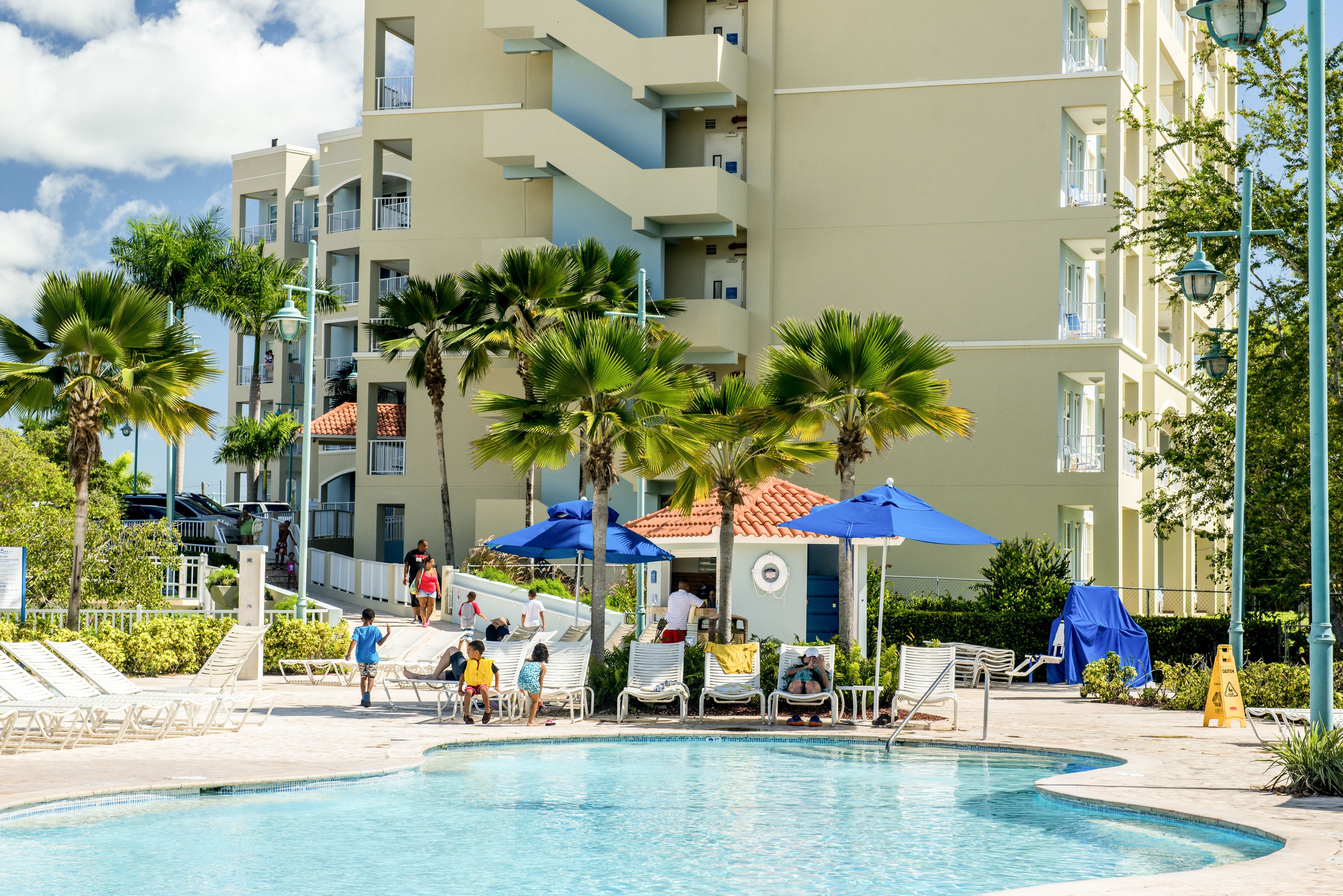 A pool area with lounge chairs, umbrellas, and a building with balconies.