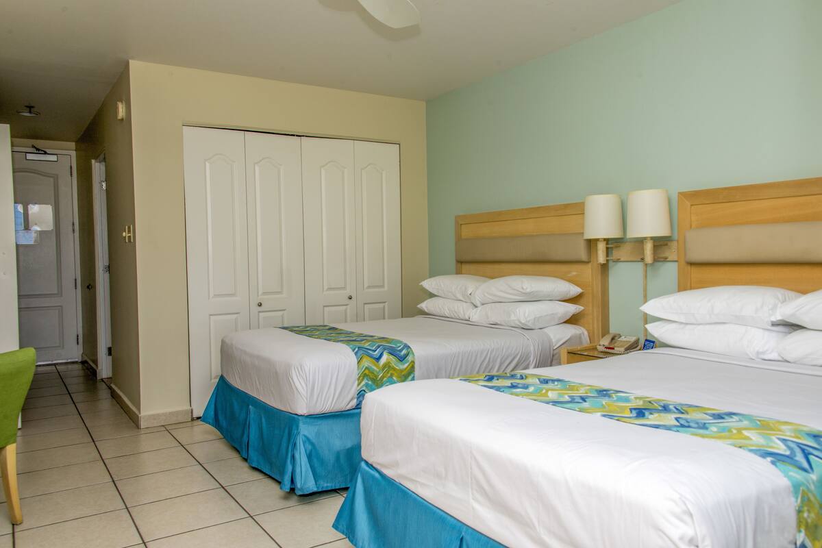 A hotel room with two beds, a wardrobe, a bedside table with lamps, and a chair.