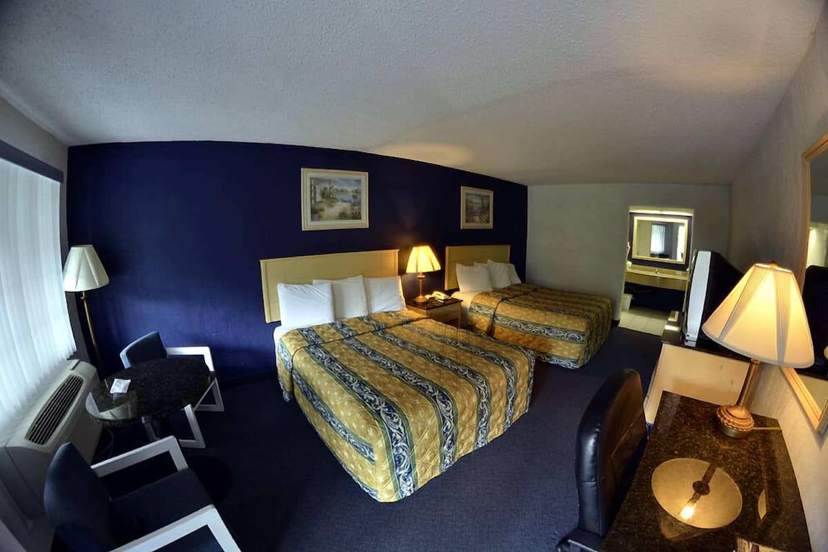 Habitación de hotel con dos camas, un escritorio, una silla, una lámpara de escritorio y un espejo.