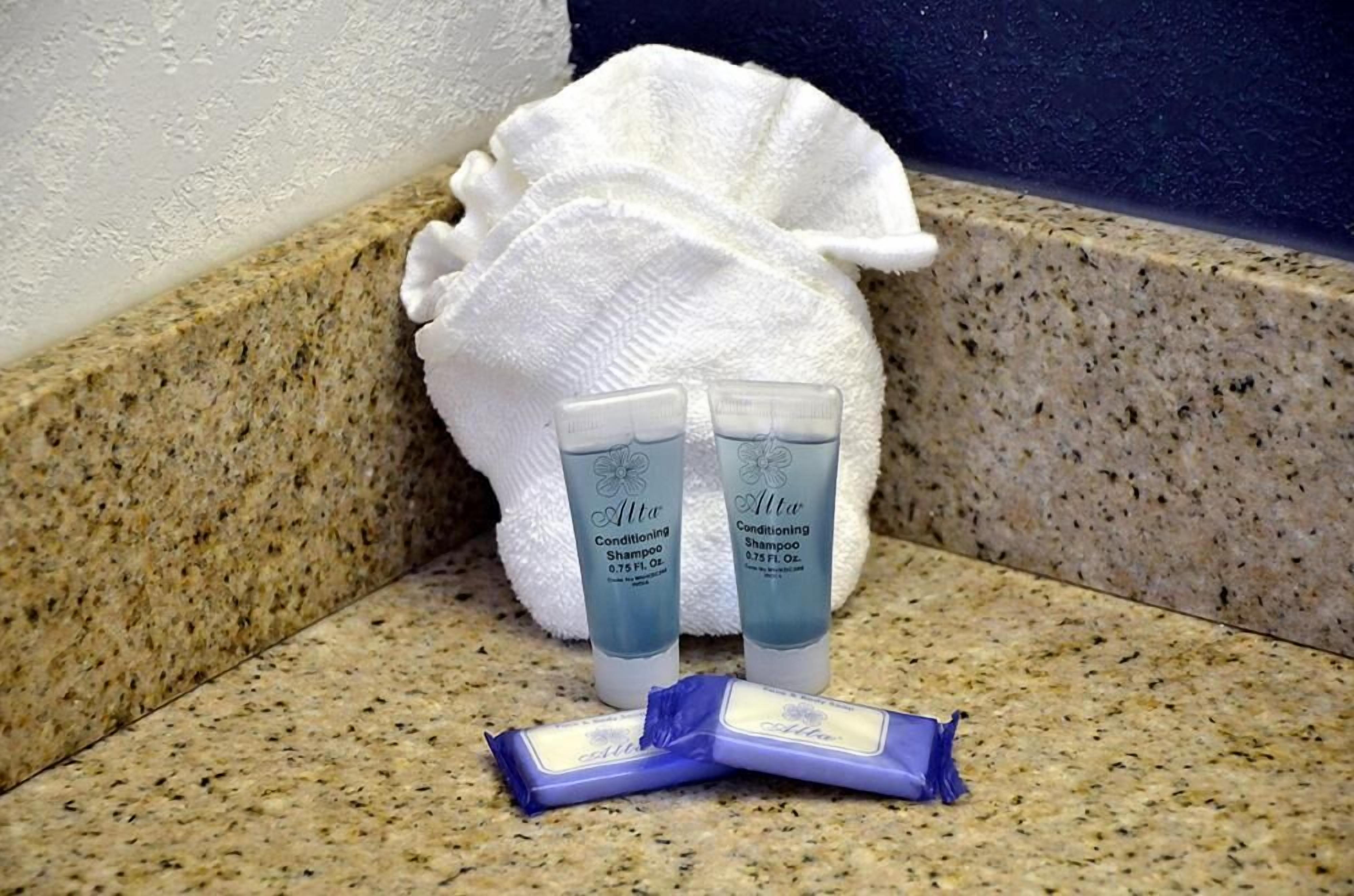 A bathroom with a white towel, two bottles of Alta Conditioning Shampoo, and a bar of soap on a granite countertop.