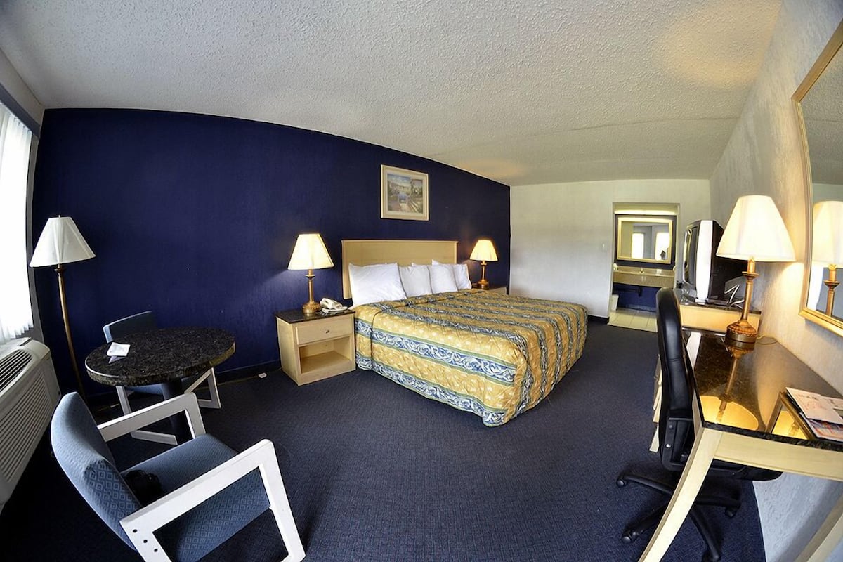 Habitación de hotel con cama, mesitas de noche, escritorio con silla, una pequeña mesa redonda y otra silla.