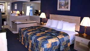 Une chambre d’hôtel avec un grand lit, un coin salon avec une chaise et une table, une baignoire et un miroir.