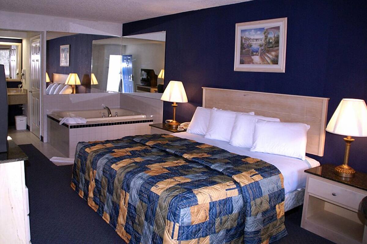 Habitación de hotel con una cama grande, un área de descanso con una silla y una mesa, una bañera y un espejo.