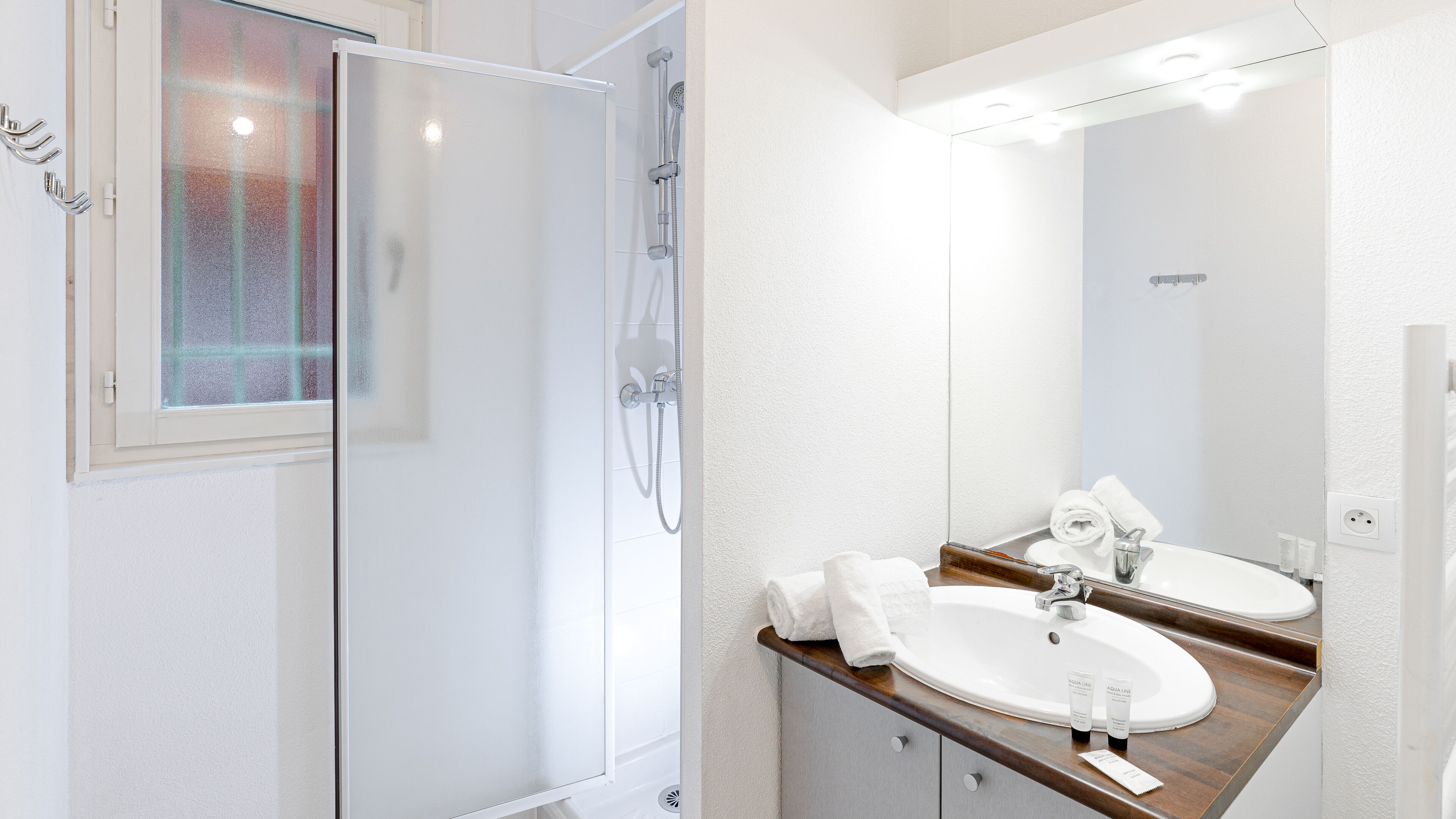 Une salle de bain moderne avec une douche à l’italienne en verre, un lavabo blanc doté d’un plan de toilette en bois et un grand miroir.
