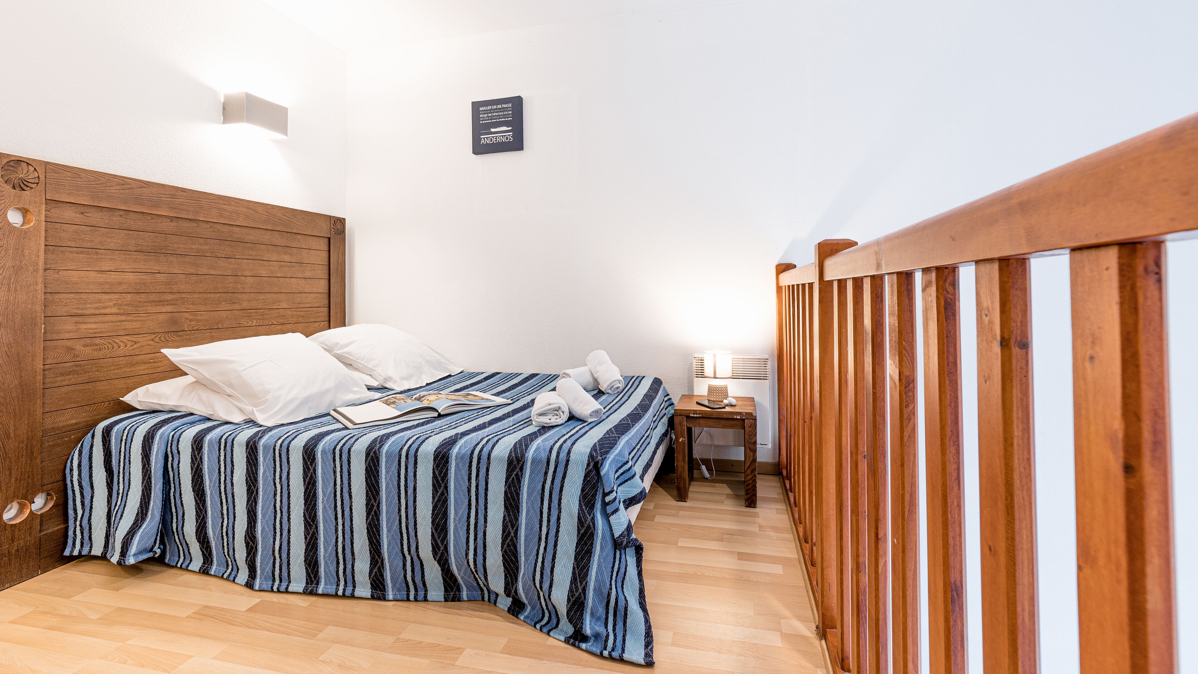 Ein Schlafzimmer mit einem Holzkopfteil, einer gestreiften Bettdecke und einem kleinen Nachttisch mit einer Lampe.