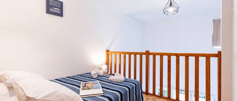 A bedroom with a wooden railing, a bed with a striped bedspread, a pillow, a bedside lamp, and a framed picture on the bed.