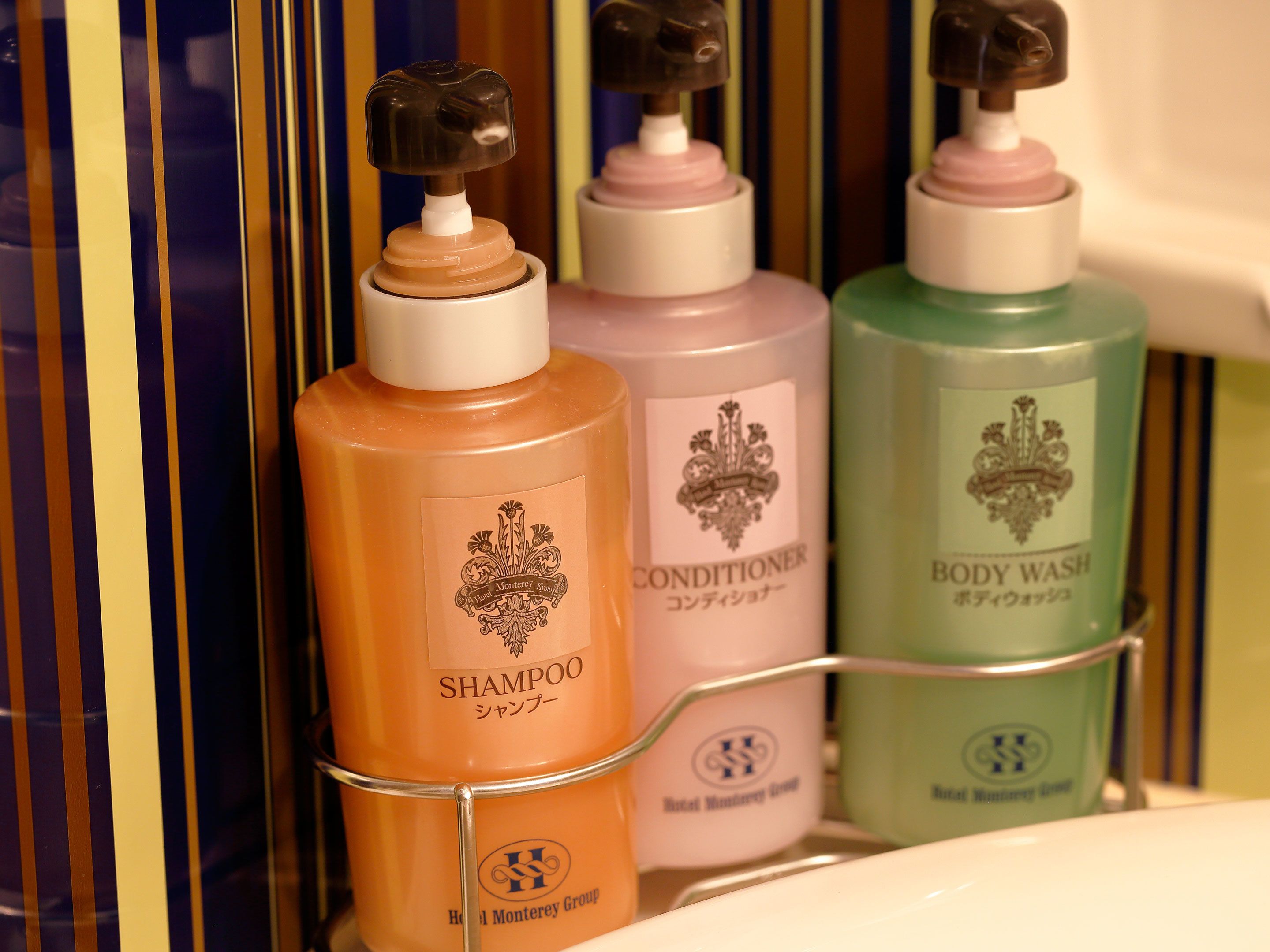 A bathroom shelf with bottles of shampoo, conditioner, and body wash from the Hotel Monterrey Group.