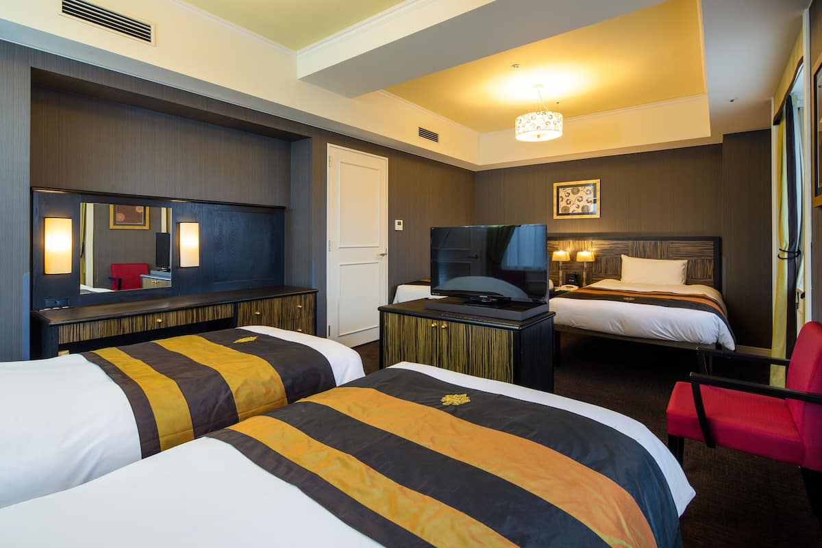 Ein Hotelzimmer mit zwei Betten, einem Fernseher, einem Schreibtisch und einem roten Sessel.
