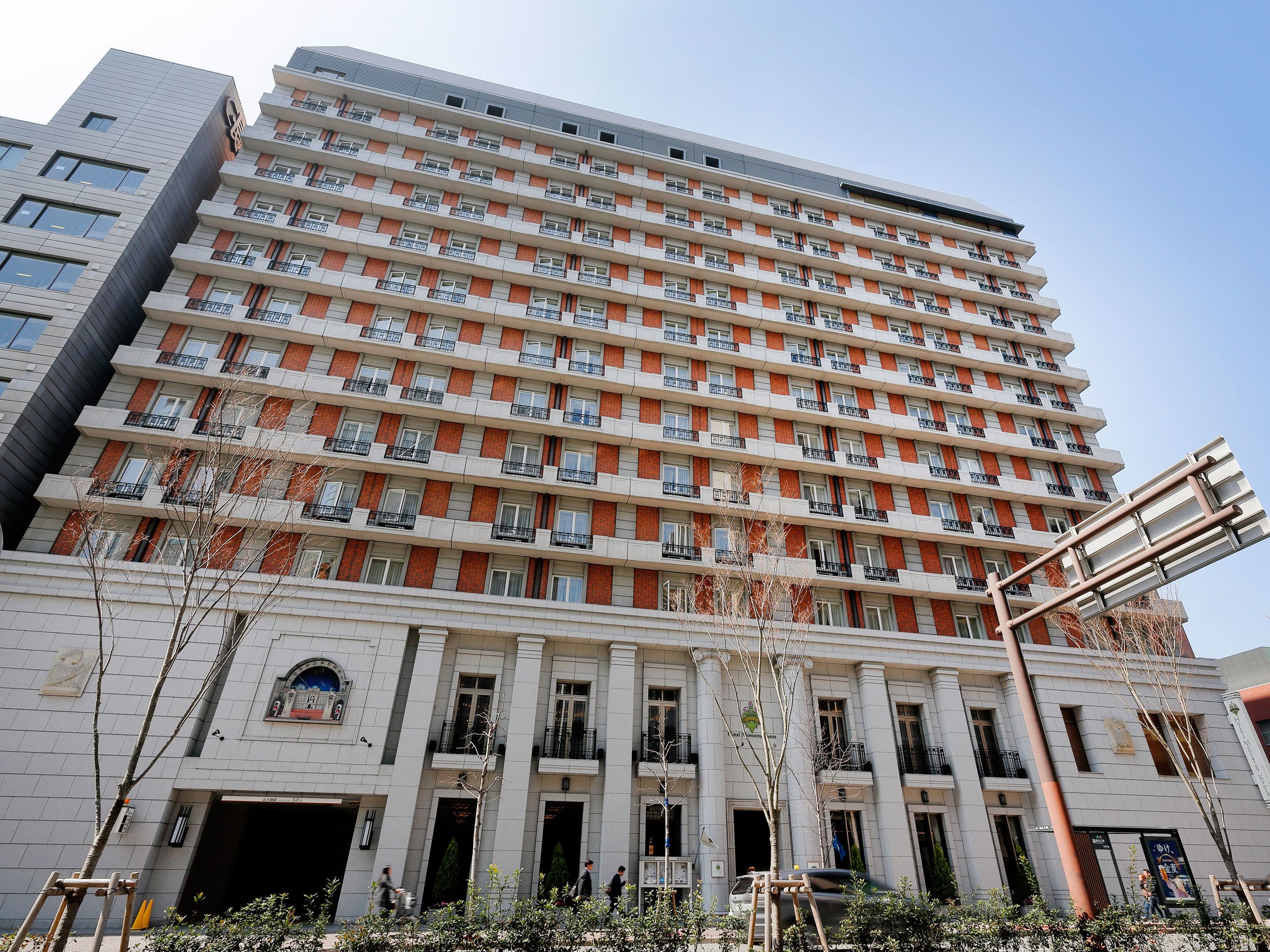 Een meerhoog hotel met een moderne gevel, bestaande uit baksteen en een witte buitenzijde, met meerdere balkons en een opvallende ingang met een grote boog.