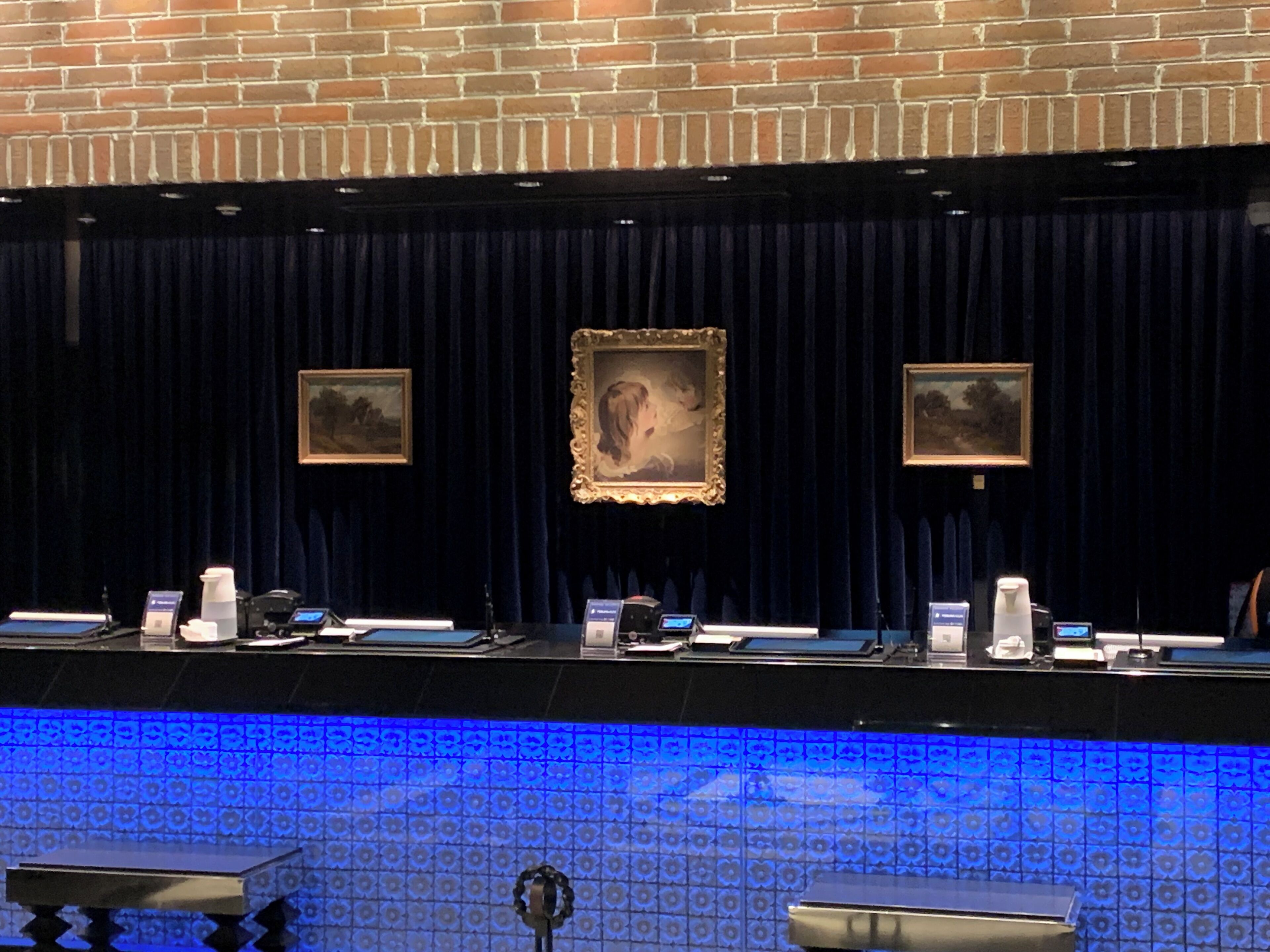 Un espace d’accueil avec un rideau sombre en arrière-plan, un sol carrelé à motifs bleus et des œuvres d’art encadrées accrochées au mur.