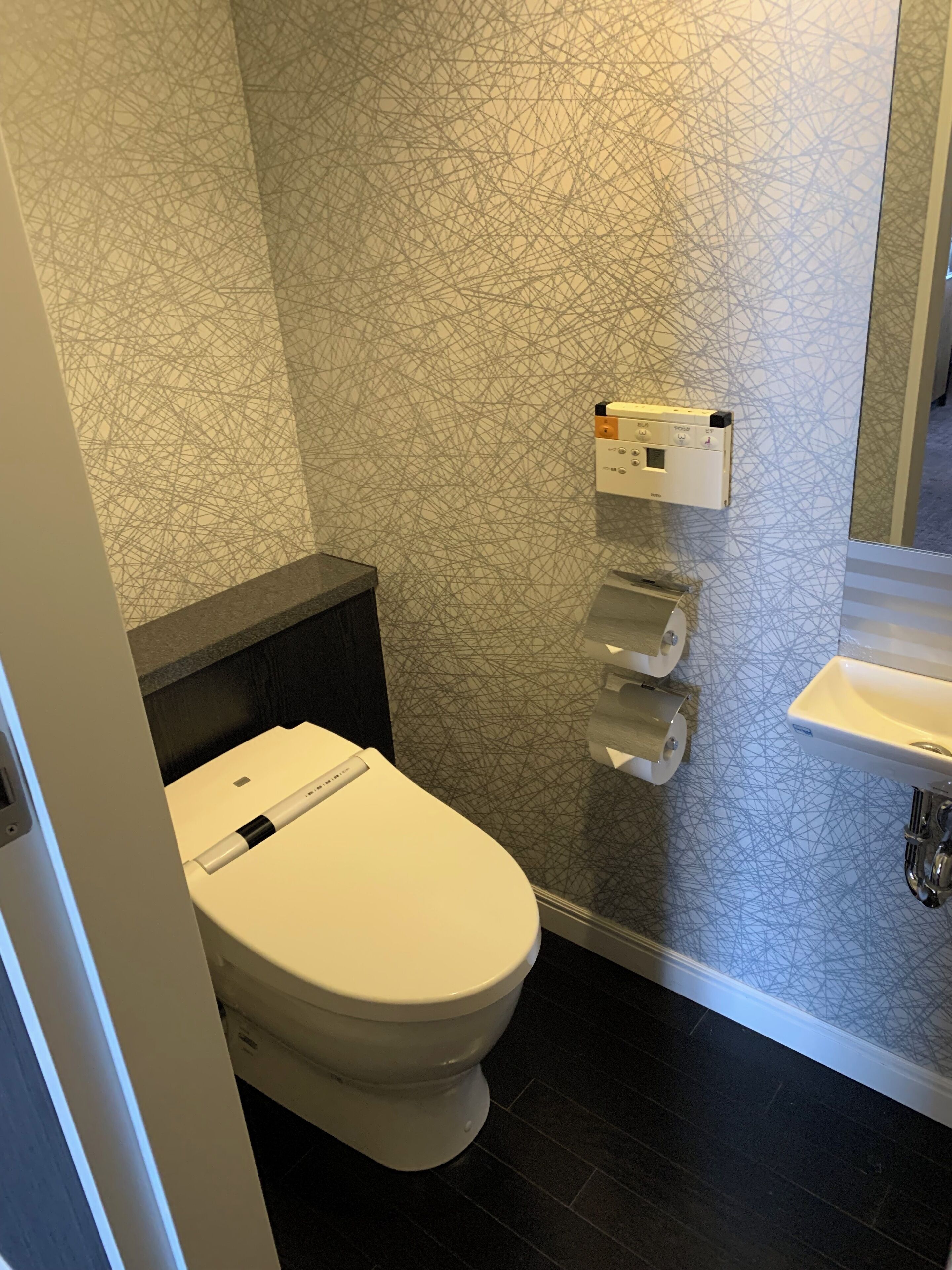 A modern bathroom with a toilet, a wall-mounted paper towel dispenser, and a sink.
