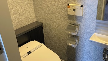A modern bathroom with a toilet, a wall-mounted paper towel dispenser, and a sink.