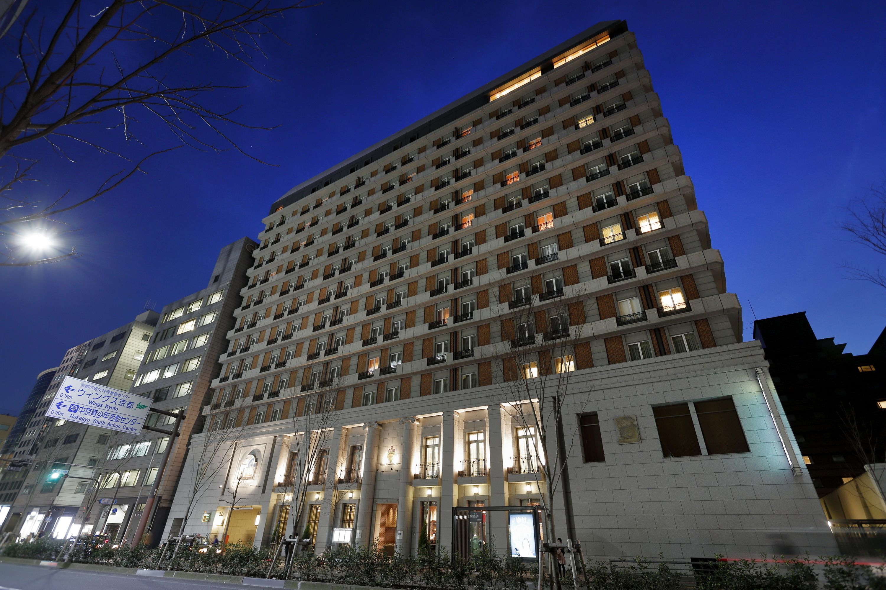 Um hotel com vários andares, entrada central, diversas varandas e fachada bem iluminada.