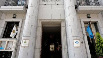 The entrance of Hotel Monterey Kyoto with a stone facade, two flags, and a sign above the entrance.